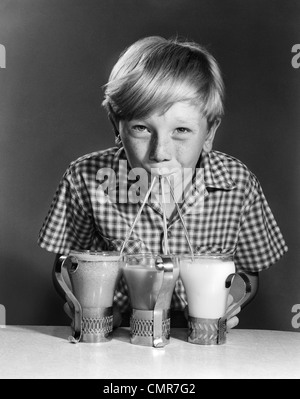 Années 1950 Années 1960 PORTRAIT DE GARÇON BLOND BOIRE AVEC DES PAILLES DE 3 MILKSHAKES SODAS SMILING AT CAMERA Banque D'Images