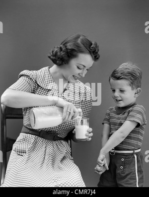 1940 WOMAN MOTHER SITTING POURING VERRE DE LAIT POUR garçon debout à côté de son fils Banque D'Images