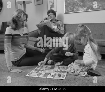 Années 1970 LA FAMILLE DE LA MÈRE DES ENFANTS QUI JOUENT LE JEU DU PLANCHER DU SALON PÈRE READING NEWSPAPER Banque D'Images