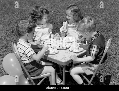 1950 PAIRE DE FILLES ET GARÇONS DE TABLE À MANGER Sur la pelouse de biscuits et de la CRÈME GLACÉE POUR ANNIVERSAIRE AVEC DES BALLONS SUR LE CÔTÉ Banque D'Images