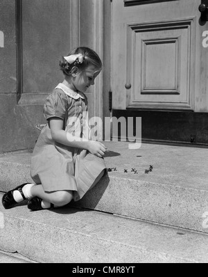 Années 1930 Années 1940 LA PETITE FILLE ASSISE SUR STOOP JOUER JACKS Banque D'Images