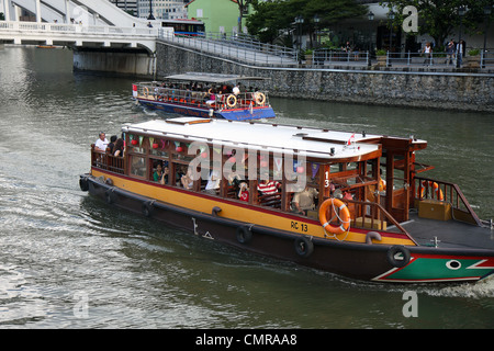 Un bateau de tourisme se déplace lentement le long de la rivière de Singapour. Banque D'Images