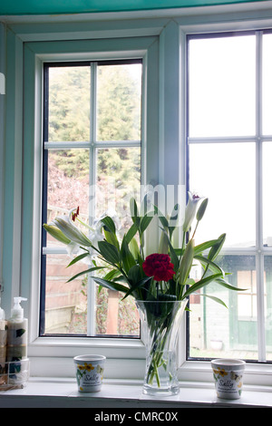 Red Carnation et lys blanc dans le vase de cristal sur le rebord de fenêtre de cuisine. Banque D'Images