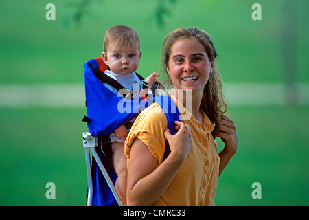 1990 MÈRE PORTANT ENFANT EN PORTE-BÉBÉ SUR SON DOS LOOKING AT CAMERA Banque D'Images