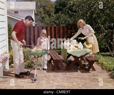 1960 famille Père Mère DEUX FILLES BARBECUE DANS JARDIN SUR PATIO DE BRIQUE Banque D'Images