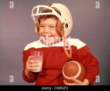 1960 garçon boire du lait portant des casques de football JERSEY ROUGE HOLDING BALL Banque D'Images