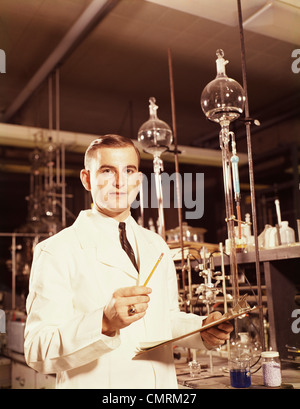 1960 MAN SCIENTIST LOOKING AT CAMERA LA RÉALISATION D'UNE EXPÉRIENCE DE CHIMIE TILRATION Banque D'Images