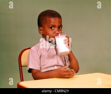 1960 1960 AFRICAN-AMERICAN BOY BOIRE DU LAIT EN VERRE LAVANDE ALIMENTAIRE NUTRITION TABLE VERRE JAUNE MAILLOT RETRO Banque D'Images