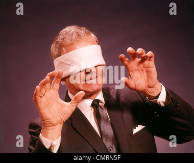 1960 1960 SENIOR BUSINESSMAN bandez les yeux bandés TENANT LES BRAS ATTEIGNENT FAÇON SENTIMENT AVEUGLE LES HOMMES VUE VISION Banque D'Images