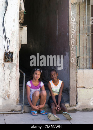 Deux jeunes enfants cubains, un garçon et une fille, s'asseoir sur le pas de la porte de l'entrée d'un studio de photographie à La Havane, Cuba. Banque D'Images