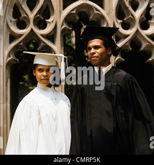 1960 AFRICAN-AMERICAN TEEN BOY AND GIRL WEARING GRADUATION ROBES Banque D'Images