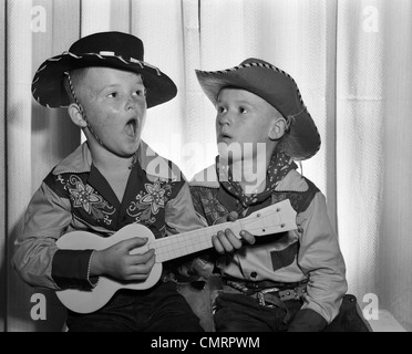 Années 50, 2 jeunes garçons en chapeau de cowboy & SHIRTS JOUER UKULELE & chanter la bouche grande ouverte Banque D'Images