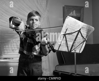 1950 garçon dans la salle de séjour pratique de violon avec expression déterminée Banque D'Images