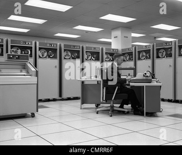 1960 MAN PROGRAMMATION TECHNICIEN ORDINATEUR CENTRAL DU CONSOLE DE LA SALLE DE CONTRÔLE ENTOURÉ PAR DE NOMBREUSES MACHINES DE STOCKAGE DE DONNÉES DU LECTEUR DE BANDE Banque D'Images