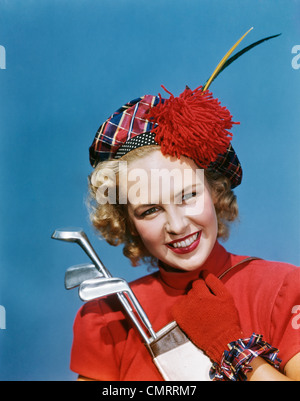 Années 1940 Années 1950 PORTRAIT SMILING BLOND WOMAN WEARING PLAID GANTS ROUGE TAM HOLDING GOLF CLUBS LOOKING AT CAMERA Banque D'Images