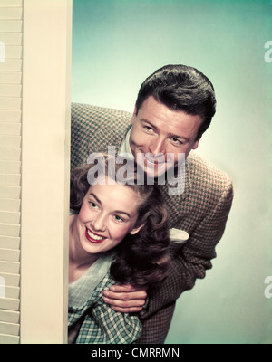 1950 SMILING COUPLE PEEKING AUTOUR DU COIN DE LA PORTE Banque D'Images