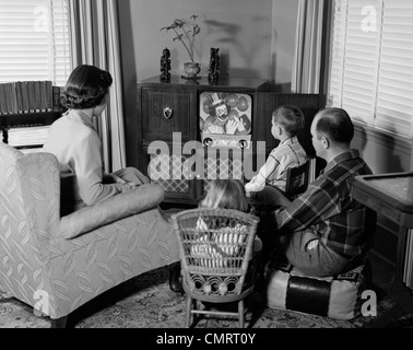 1950 VUE ARRIÈRE DE FAMILLE DE 4 RÉUNIS AUTOUR DE REGARDER LA TÉLÉVISION AVEC DES BALLONS CLOWN Banque D'Images