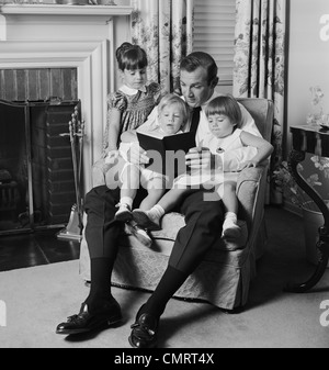 1970 HOMME PÈRE ASSIS DANS UN FAUTEUIL AVEC TROIS ENFANTS READING BOOK Banque D'Images