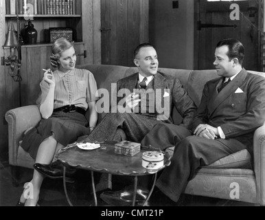 Années 1930 Années 1940 DEUX HOMMES ET UNE FEMME DE GROUPE SOCIAL PARLE DE FUMER DES CIGARETTES Banque D'Images