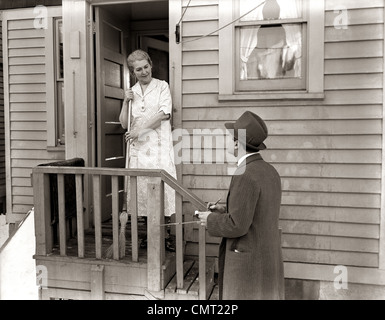 1940 1930 MAN PORTE-À-PORTE, SALESMAN TALKING FEMME À FEMME AU FOYER À PORTE ARRIÈRE Banque D'Images