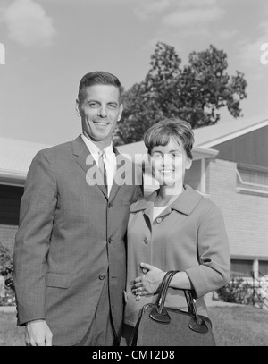 1960 PORTRAIT SMILING COUPLE IN FRONT OF SUBURBAN HOUSE Banque D'Images