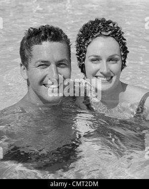 1960 SMILING COUPLE MAN WOMAN IN SWIMMING POOL Banque D'Images