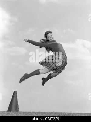 1960 CHEERLEADER EN Jupe à carreaux PULL CHAUSSETTES & sautant dans l'AIR HAUT LOOKING AT CAMERA Banque D'Images