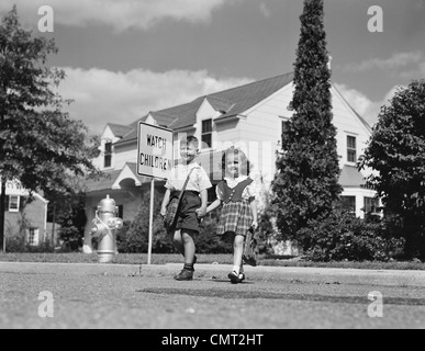 Années 1940 Années 1950 BOY GIRL HOLDING HANDS CROSSING STREET ALLER À L'ÉCOLE LES ENFANTS REGARDER SIGNER Banque D'Images