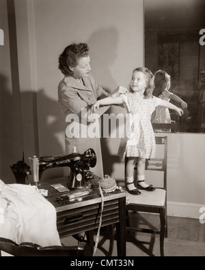 1950 MÈRE DE RÉGLAGE ACCUEIL COUSU SUR ROBE FILLE PAR MACHINE À COUDRE, Banque D'Images