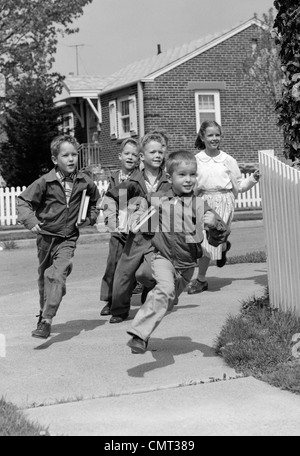 1950 GROUPE D'ENFANTS DE L'ÉCOLE TOURNANT AUTOUR DU COIN DU QUARTIER DE BANLIEUE EN CLÔTURE Banque D'Images