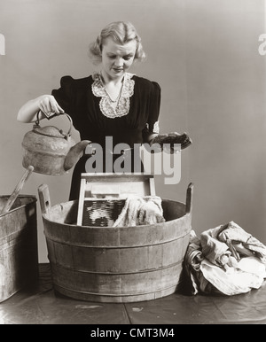 1940 mécontent de verser de l'eau ménagère ÉLECTRIQUE DANS LE SEAU AVEC WASHBOARD et serviettes Banque D'Images