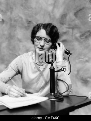 Années 1920 Femme portant des lunettes pince-nez SITTING AT DESK TALKING ON PHONE Chandelier Banque D'Images