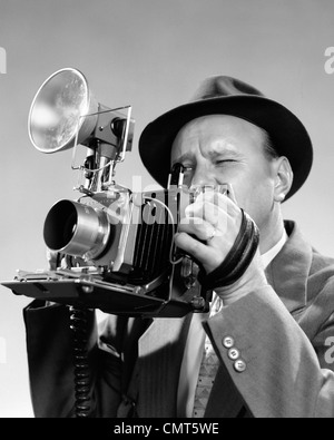 1950 PORTRAIT DE PHOTOGRAPHE MAN IN SUIT ET FEDORA HAT en plissant les yeux pour regarder à travers le viseur de l'appareil photo de presse Banque D'Images