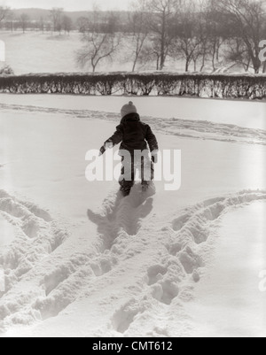 1950 VUE ARRIÈRE ENFANT EN HABIT DE PRENDRE LES PISTES dans la neige fraîche Piscine Banque D'Images