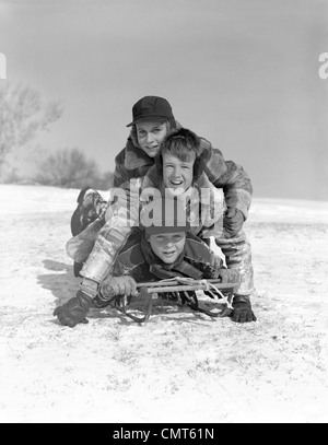 1950 Trois garçons empilé sur traîneau sur la colline couverte de neige OUTDOOR LOOKING AT CAMERA Banque D'Images