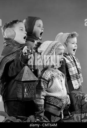 Années 1950, quatre enfants deux garçons deux filles chanter Noël ensemble HOLDING lanterne à bougie Banque D'Images