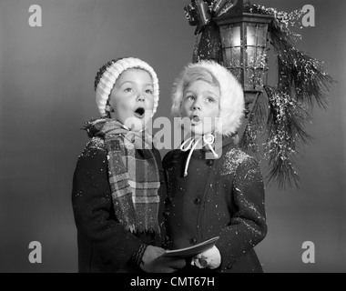 1960 BOY AND GIRL SINGING CHRISTMAS CAROL ENSEMBLE SOUS LA LUMIÈRE porche extérieur enneigé Banque D'Images