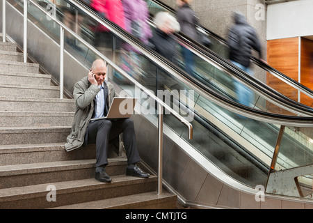 L'homme dans les escaliers à l'aide d'ordinateur portable et téléphone cellulaire Banque D'Images