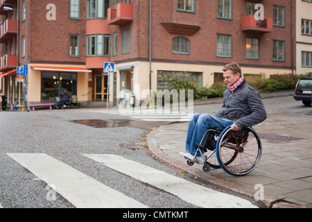 Man in wheelchair crossing road Banque D'Images