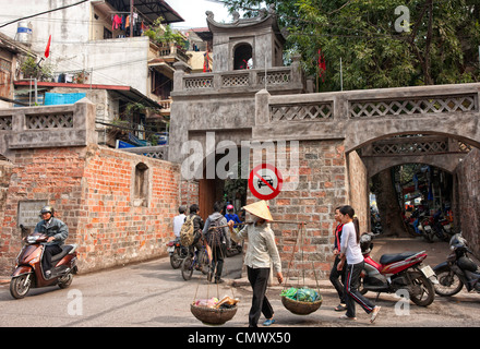 Vendeur alimentaire carry wares passé, ancienne porte de la ville et le mur à Hanoi Banque D'Images