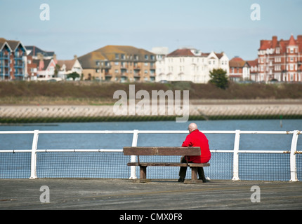 Un homme dans une veste rouge assis sur un banc sur Clacton Pier, sur la côte d'Essex. Banque D'Images