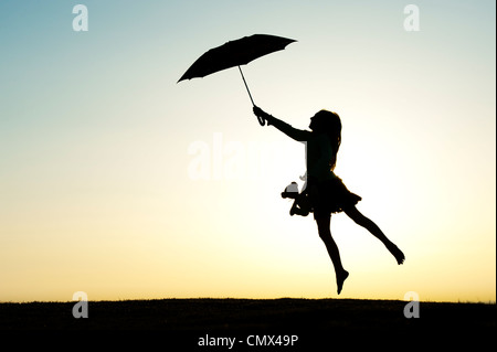 Jeune fille sautant avec un parapluie et ours au coucher du soleil. Silhouette. UK Banque D'Images