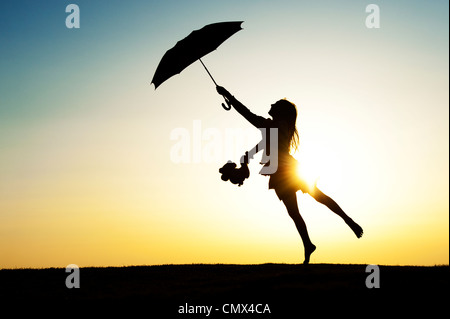 Jeune fille sautant avec un parapluie et ours au coucher du soleil. Silhouette. UK Banque D'Images