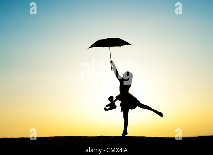 Jeune fille sautant avec un parapluie et ours au coucher du soleil. Silhouette. UK Banque D'Images