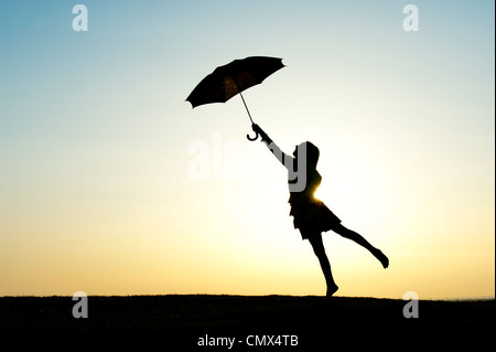 Jeune fille sautant avec un parapluie au coucher du soleil. Silhouette Banque D'Images