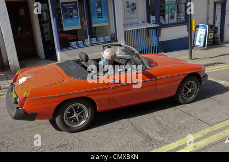 Un homme aux cheveux gris dans la soixantaine avancée attend au feu dans une voiture sport décapotable Banque D'Images