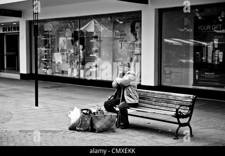 Vieil homme assis seul sur un banc avec shopping centre ville Banque D'Images