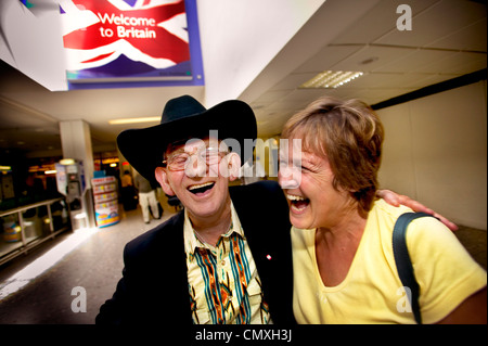 Rire passagers à la porte d'arrivée à l'aéroport de Heathrow avec en arrière-plan de l'affiche annonçant "bienvenue à Bretagne' Banque D'Images