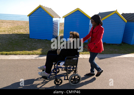 United Kingdom West Sussex arundel une femme âgée dans un fauteuil roulant à roues en cours des cabanes de plage Banque D'Images