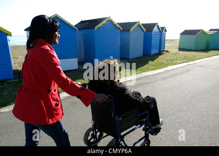 United Kingdom West Sussex arundel une femme âgée dans un fauteuil roulant à roues en cours des cabanes de plage Banque D'Images